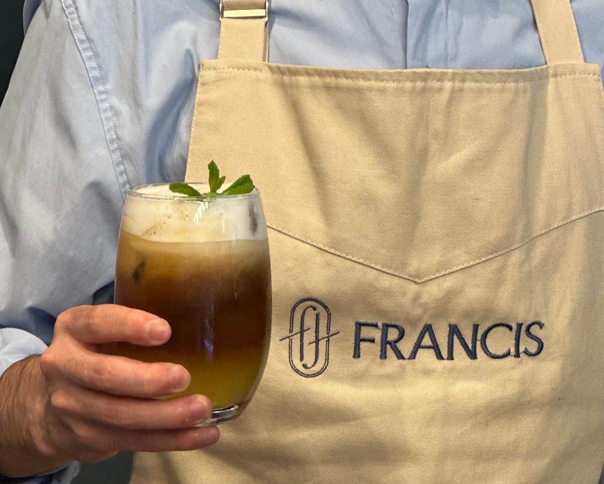 Delantal de Francis con el imagotipo, sosteniendo un café frío