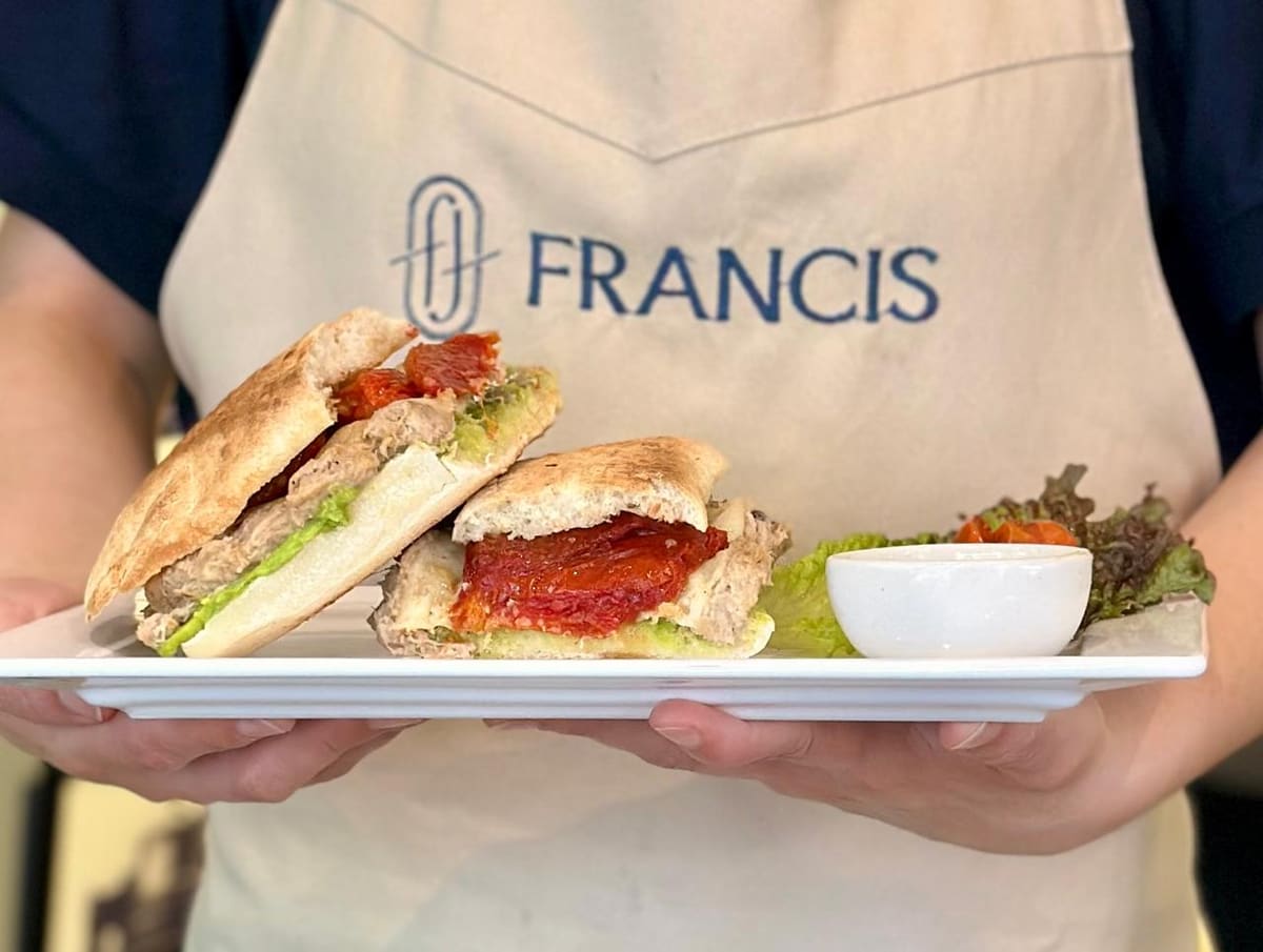 Delantal de Francis con el imagotipo bordado, llevando un plato de sándwiches