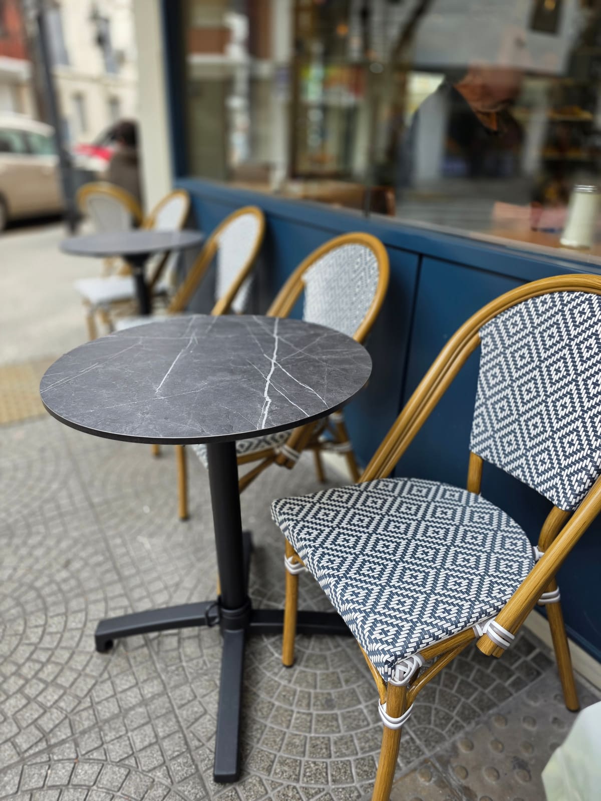 Mesa de mármol y sillas de rattan trenzado en blanco y azul, en la vereda de Francis